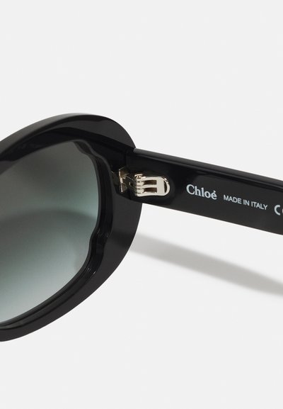 Zwarte zonnebril met oversized glazen en een gradient tint. Heeft een glanzend plastic montuur en een zilveren scharnier, gegraveerd met "Chloé MADE IN ITALY."