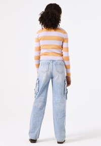 Jersey de rayas en naranja y lavanda, combinado con unos vaqueros cargo en denim azul claro, con bolsillos laterales y corte holgado, visto desde la espalda.