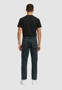 Maglietta nera, jeans in denim scuro con tasche cucite, vestibilità rilassata e sneaker bianche. Focus sulla semplicità e sul comfort nel design.