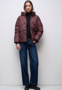 Vínová prošívaná bunda s kapucí, diagonálním prošíváním, kapsami na zip a staženým pasem, doplněná tmavě modrými džínami s širokými nohavicemi.
