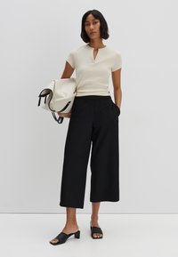 Beige ribbed top with a keyhole neckline, paired with black wide-leg trousers, holding a cream bag with black accents, and wearing black block-heeled slides.