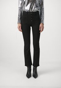 Vysoké černé džíny s mírně rozšířeným střihem, se zapínáním na pět knoflíků a dvěma předními kapsami. Nosí se s černými špičatými kotníkovými botami.