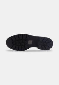 Semelle de chaussure en caoutchouc noir avec des rainures profondes et un petit logo rectangulaire au centre sur fond blanc.