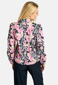 Kwiatowa bluzka z granatowym tłem, różowymi i żółtymi kwiatowymi wzorami, długimi rękawami i plisowanym tyłem.