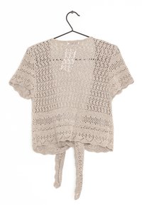 Beige kortärmad virkade topp med öppet mönster, vågiga kanter och två hängande band bak på en svart galge.