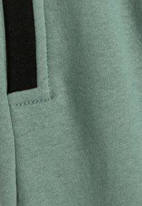 Mintgrüner Stoff mit einer weichen Textur, verziert mit einem schwarzen Akzentstreifen entlang des Randes und sauberen Nähten. Einfaches und funktionales Design.