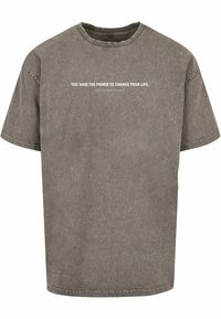 Grijze oversized t-shirt van zachte katoen met een ronde hals. Heeft een witte geprinte tekst over de borst. Eenvoudig ontwerp, geen patronen.