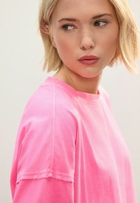 Felroze oversized t-shirt met een ribbelkraag, korte mouwen en zichtbare stikdetails. Zachte katoenen stof met een gladde textuur.