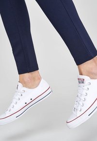 Witte canvas sneakers met rode en blauwe accenten, ronde neus en vetersluiting. Draag met marineblauwe enkelbroek, waarbij een deel van het been zichtbaar is.