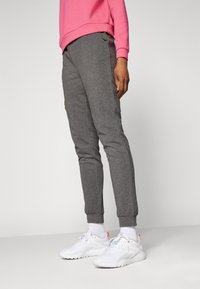 Grå joggebukser i en tapered passform, med elastiske mansjetter, sidelommer og en subtil logo. Kombinert med hvite joggesko og hvite sokker.