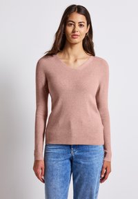 Světle růžový svetr s výstřihem do V, s žebrovanou strukturou a dlouhými rukávy, kombinovaný s džínami. Jednoduchý, přiléhavý design.