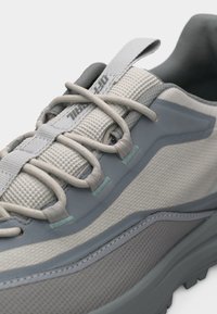 Ανοιχτό γκρι και μπλε αθλητικό παπούτσι με υφασμάτινη υφή, κορδόνια με θηλιές και επενδεδυμένο γιακά, εμφανιζόμενο σε κοντινή λήψη από το πλάγιο επάνω μέρος.