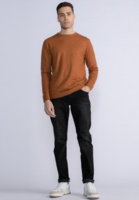 Maglione testurizzato arancione bruciato abbinato a jeans slim-fit neri e sneakers bianche, con polsini a coste e scollatura classica a girocollo.