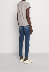 Grå t-shirt med kort ärm, blå denimjeans och vita sneakers med gröna detaljer. T-shirten har en avslappnad passform och en något rundad nederkant.