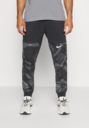 Schwarze Jogginghose mit strukturiertem grauem Tarnmuster, elastischen Bündchen und kleinem weißem Nike-Logo am linken Oberschenkel.