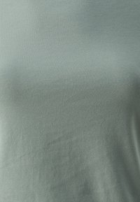 Világoszöld, rövid ujjú felső, sima, rugalmas anyagból készült, bordázott textúrával és laza szabással. Nincsenek látható minták vagy díszítések.