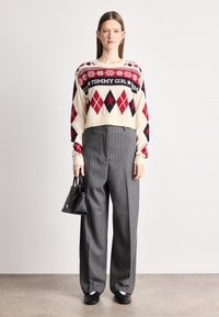 Fehér és piros, rombusz mintás, rövidített pulóver, szürke csíkos, bő szárú nadrággal párosítva. A fekete táska és cipők teszik teljessé a megjelenést.