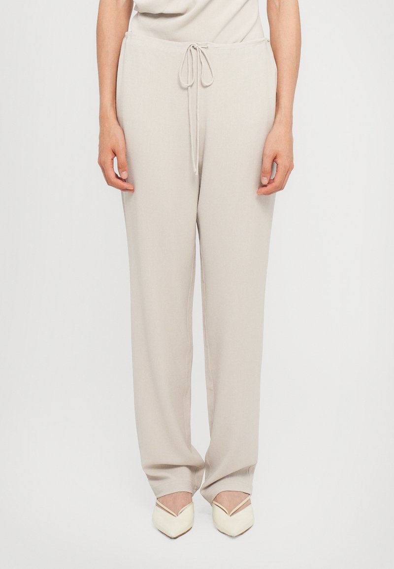Lichtbeige wijde broek met een trekkoord in de taille, een soepele textuur en een ontspannen pasvorm, gecombineerd met witte schoenen met een puntige neus.
