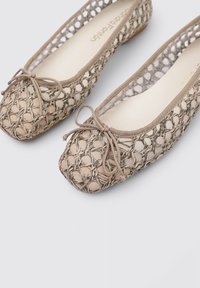 Bailarinas de yute beige con un diseño de malla texturizada, puntera redondeada y un lazo de tela en la parte delantera. Forro interior suave y tacón bajo.