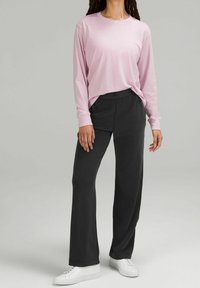 Långärmad rosa topp i kombination med löst sittande svarta byxor. Outfiten har en mjuk textur och kompletteras av vita sneakers.