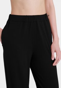 Pantaloni neri con elastico in vita, realizzati in tessuto morbido, caratterizzati da una vestibilità comoda e tasche laterali, con una texture liscia e un design minimalista.