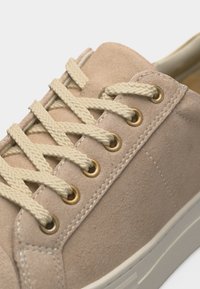 Baskets en suède beige avec des lacets plats couleur crème passant à travers six paires d'œillets métalliques sur une semelle blanche.