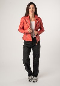 Rode leren, aansluitende motorjacks met zilver hardware en gedetailleerde stitching; gecombineerd met zwarte broek en sneakers.