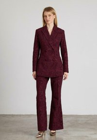 Bordeaux, gestructureerd pak bestaande uit een dubbele-breasted blazer met ingeknipte revers en uitlopende broeken. Gecombineerd met metallic hakken.