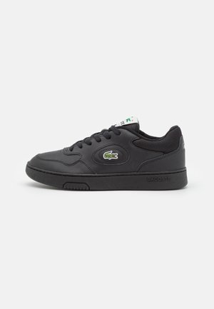 Basket noir basse avec semelle texturée, lacets noirs et logo crocodile vert de Lacoste sur le côté et la languette.
