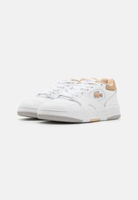 Chaussures de sport blanches avec une tige en cuir, un talon en suede beige contrastant, bout rond, col rembourré et semelle en caoutchouc avec des stries horizontales.