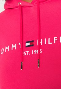 Roze katoenen hoodie met het geborduurde logo "TOMMY HILFIGER" en "EST. 1985" in het wit, met zilverkleurige uiteinden aan de trekkoorden.