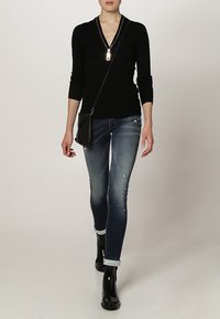 Czarny sweter zapinany na zamek i przetarte niebieskie dżinsy, w połączeniu z błyszczącymi czarnymi botkami za kostkę. Kompaktowa czarna torba na ramię z paskiem.