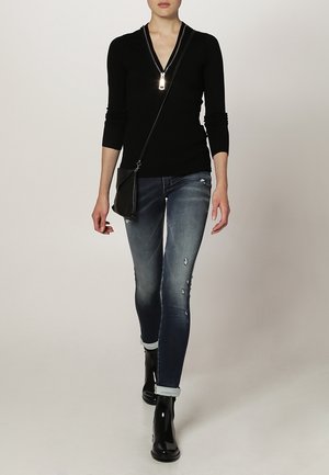 Czarny sweter zapinany na zamek i przetarte niebieskie dżinsy, w połączeniu z błyszczącymi czarnymi botkami za kostkę. Kompaktowa czarna torba na ramię z paskiem.