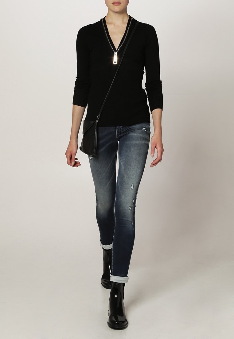 Czarny sweter zapinany na zamek i przetarte niebieskie dżinsy, w połączeniu z błyszczącymi czarnymi botkami za kostkę. Kompaktowa czarna torba na ramię z paskiem.