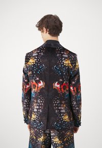 Patterned blazer and pants in black velvet, featuring colorful butterfly motifs in blue, orange, and yellow. Tailored design with a notch lapel.