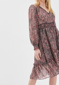 Robe à motif floral en tissu léger avec un décolleté en V, des manches longues bouffantes et une taille élastique. Comprend un ourlet froncé et des accents noirs.