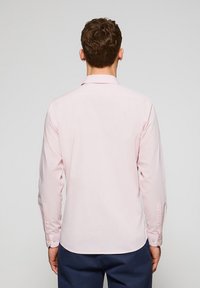 Camicia a maniche lunghe in cotone rosa chiaro, con colletto classico e dettagli dei polsini a bottone, vista da dietro. Texture liscia.