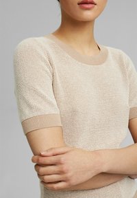 Beige lyhythihainen neulepaita, jossa on teksturoitu kuvio, kontrastiväriset ribbireunat ja pyöreä kaula-aukko. Sileä kangas ja kapea malli.