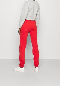 Red sweatpants in a relaxed fit, made of soft fabric, featuring an elastic waistband and cuffed ankles. Paired with a gray sweatshirt and white sneakers.