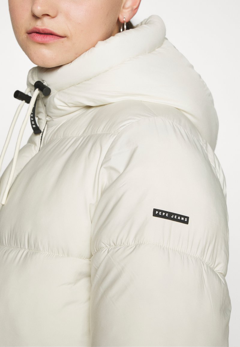 Chaqueta acolchada blanca con un cuello alto, que incluye una capucha con cordón. Presenta un logo negro de "Pepe Jeans" en la manga. Textura suave.