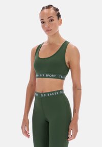 Žalias sportinis liemenėlis ir derančios tamprės iš tamprios audinio medžiagos. Yra platus elastinis diržas su užrašu „TED BAKER SPORT“ baltais rašmenimis.