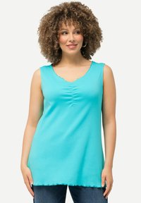 Top sin mangas en aqua con escote festoneado y detalle fruncido en el centro. Textura suave y corte holgado, combinado con jeans oscuros.