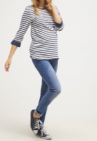 Camiseta de manga larga a rayas en blanco y azul marino, combinada con pantalones vaqueros ajustados azules y zapatillas de deporte azul marino. Presenta un corte relajado y un dobladillo redondeado.