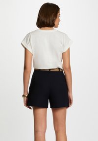 White short-sleeve blouse with rolled cuffs paired with black high-waisted shorts, featuring a brown belt and side pockets.