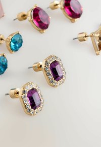 Gold-tone stud earrings featuring a purple faceted stone surrounded by clear rhinestones, alongside various other colorful gemstone studs.