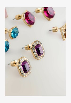 Złote sztyfty z fioletowym fasetowanym kamieniem otoczonym przez przezroczyste cyrkonie, obok różnych innych kolorowych kamieni sztyftów.