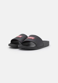 Black slide sandals with a matte finish, featuring a wide strap with a red Levi's logo. Textured footbed and durable rubber sole.