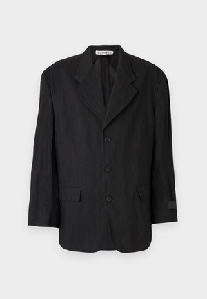 Schwarzer Blazer aus strukturiertem Stoff, mit einem Reverskragen, sechs Knöpfen und zwei Taschen. Der linke Ärmel verfügt über ein Etikett-Detail.