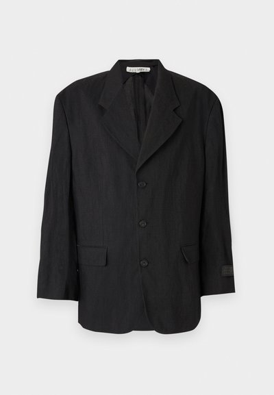 Blazer negro de tela texturizada, con solapa en muesca, seis botones y dos bolsillos. La manga izquierda tiene un detalle de etiqueta.
