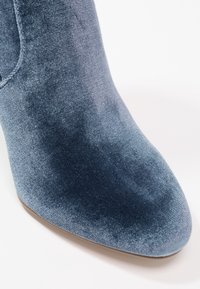 Modré sametové kotníkové boty s špičatou špičkou a hladkým povrchem, se jemným žebrováním a elegantním, těsným designem.